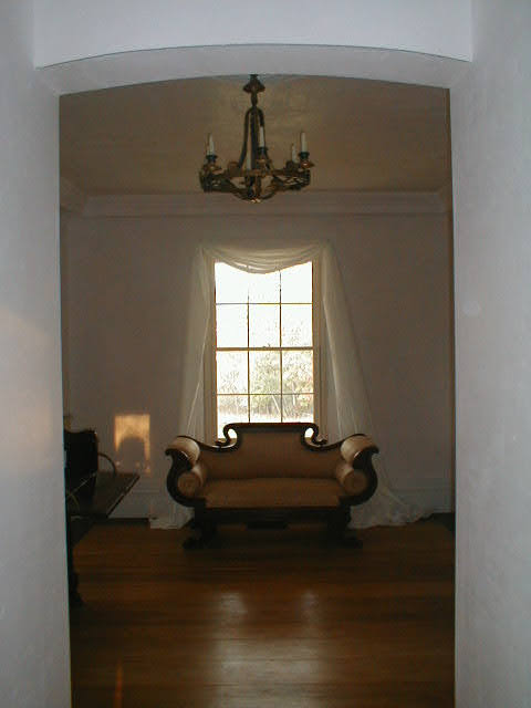 Second-floor hall seen through curved archway, Empire sofa under tall window with sheer curtains